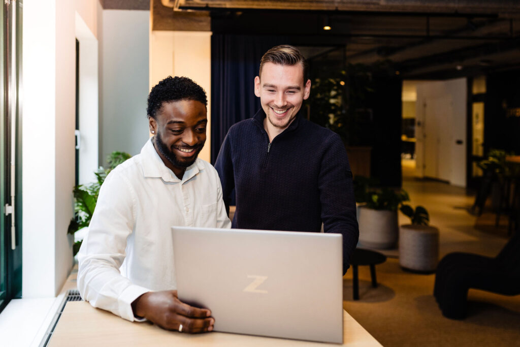 Twee consultants bekijken samen een laptop in een kantooromgeving.